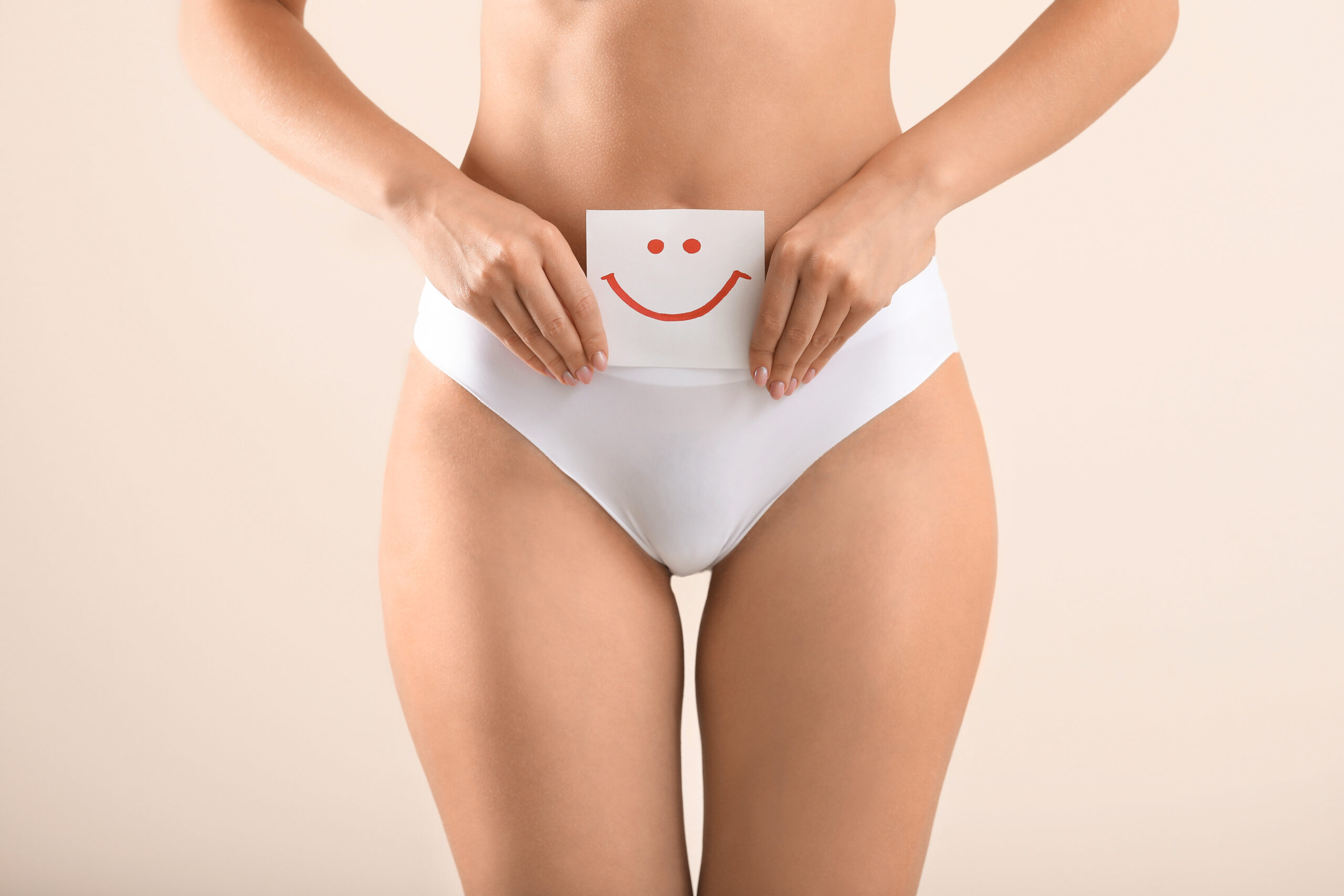 Young woman holding paper with drawn happy emotion on light background. Gynecology concept